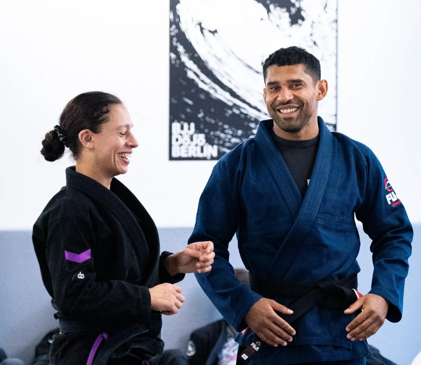 Zwei Coaches lachen gemeinsam im Gi auf der Matte des BJJ DOJO Berlin in Kreuzberg. Foto: Photo Blackbelt.